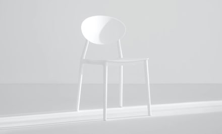 Minimalist white chair highlighted by soft lighting in a bright setting.
