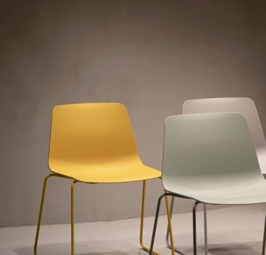 Set of modern chairs in yellow, light green, and white, arranged in a neutral space.